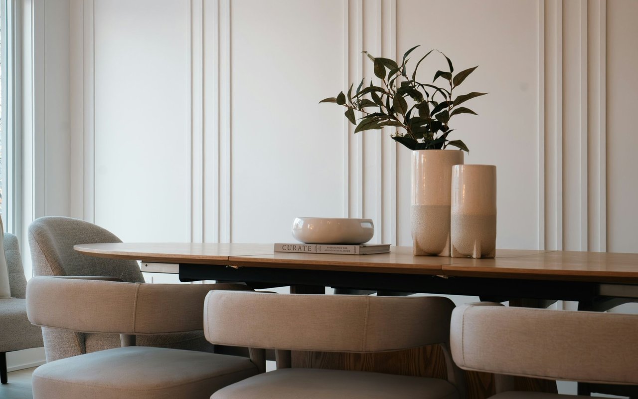 Dining room with a long wood table, upholstered chairs, and ceramic vases.