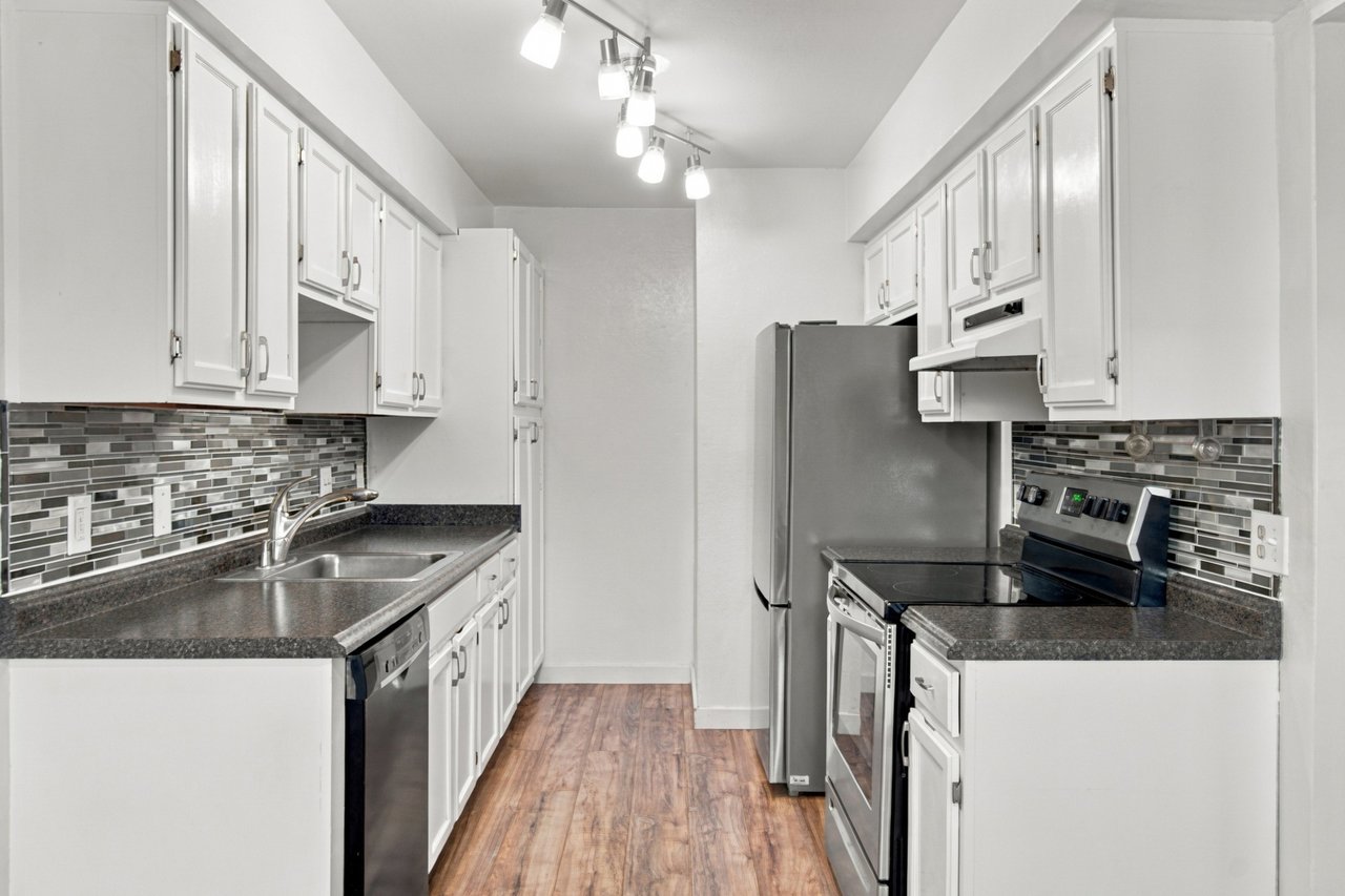 Galley kitchen with white cabinets, stainless steel appliances, and a gray mosaic backsplash.