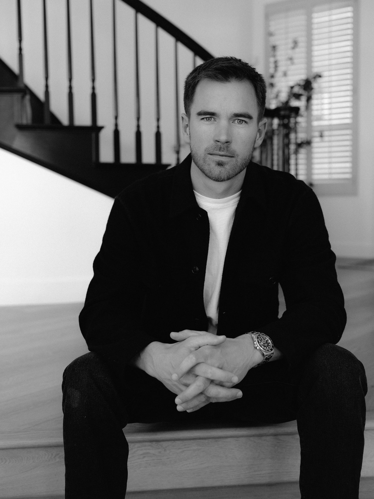 Abe Fark seated with clasped hands in front of a staircase.