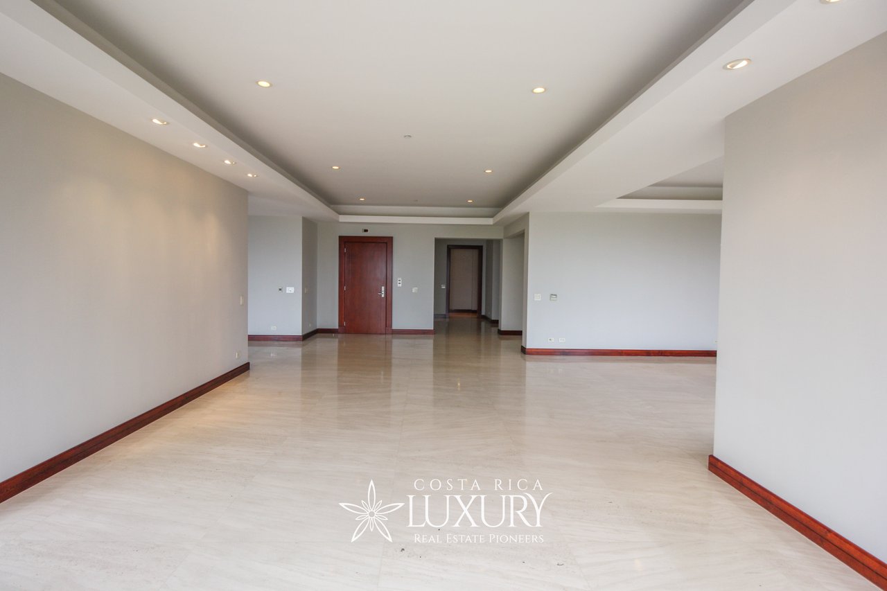 Empty apartment living area with glossy stone floors, dark wood trim, and recessed ceiling lights.