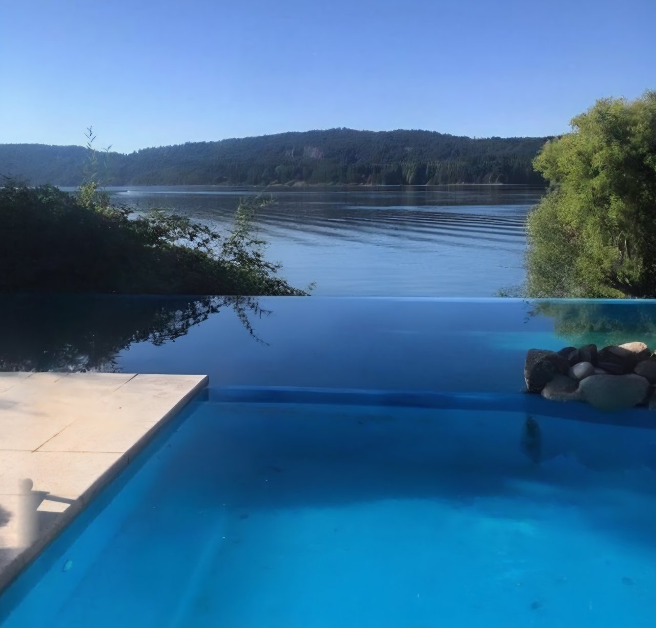 Infinity pool overlooking a lake and forested hills, with a pale stone deck.