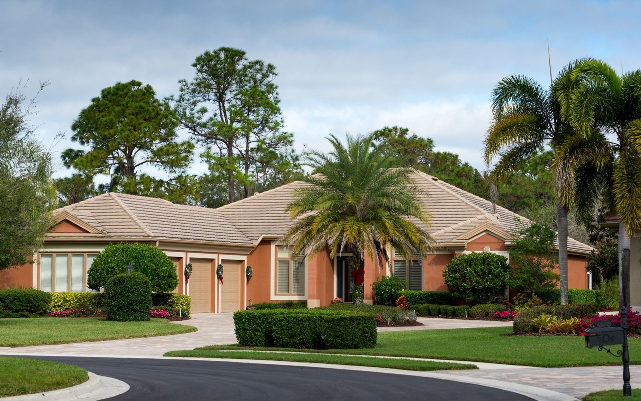 Single-story peach stucco home with a tile roof, palm trees, and a landscaped front yard.