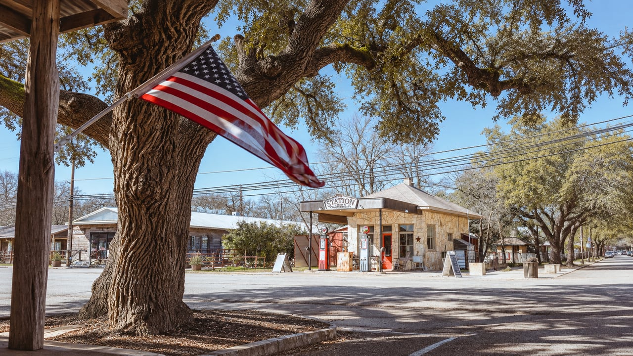 A stone station storefront sits beneath a large oak beside an American flag.