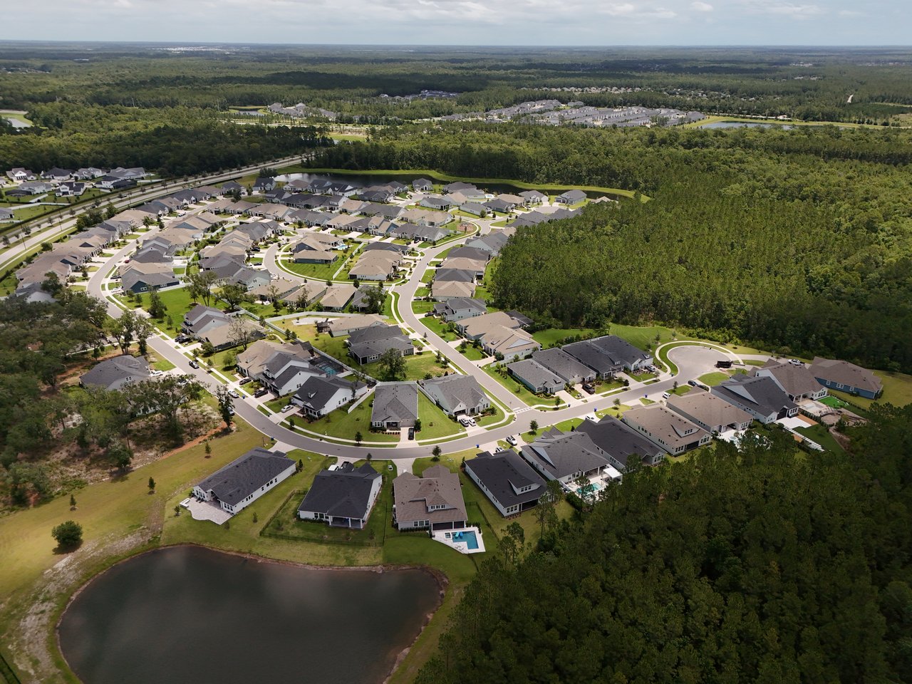 Aerial view of Oak Grove homes beside a pond, with wooded land surrounding the neighborhood.