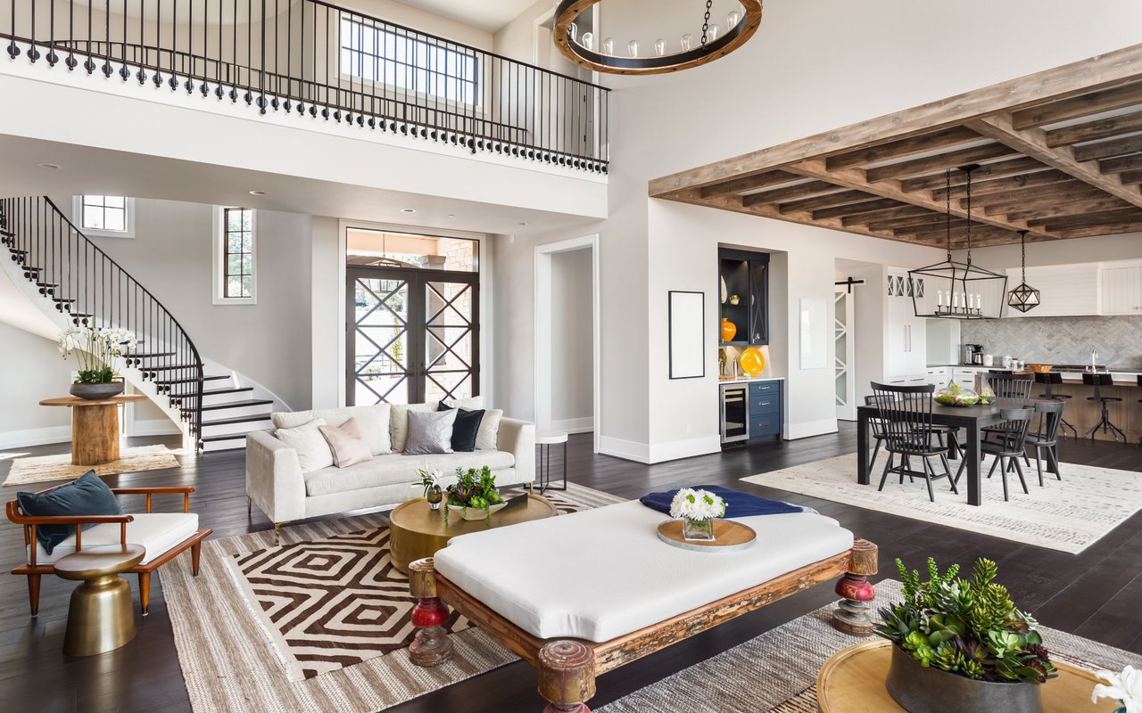 Open-plan living room with a curved staircase, white sofa, and exposed timber ceiling beams.