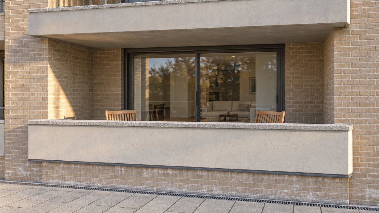 Close exterior view of a buff-brick condominium with recessed concrete balconies and bronze-framed glass doors in late-afternoon light.