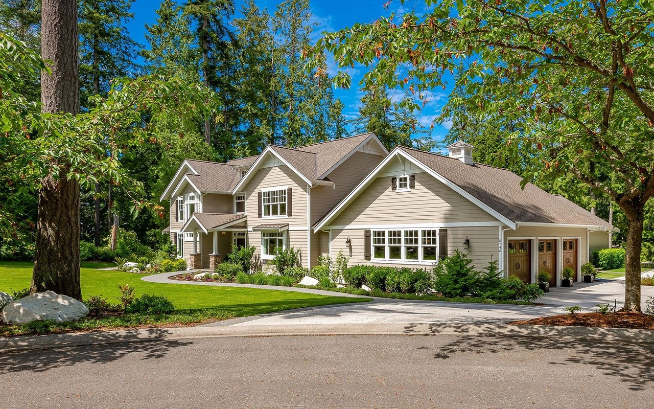 Large beige two-story house with an attached three-car garage, surrounded by mature trees.