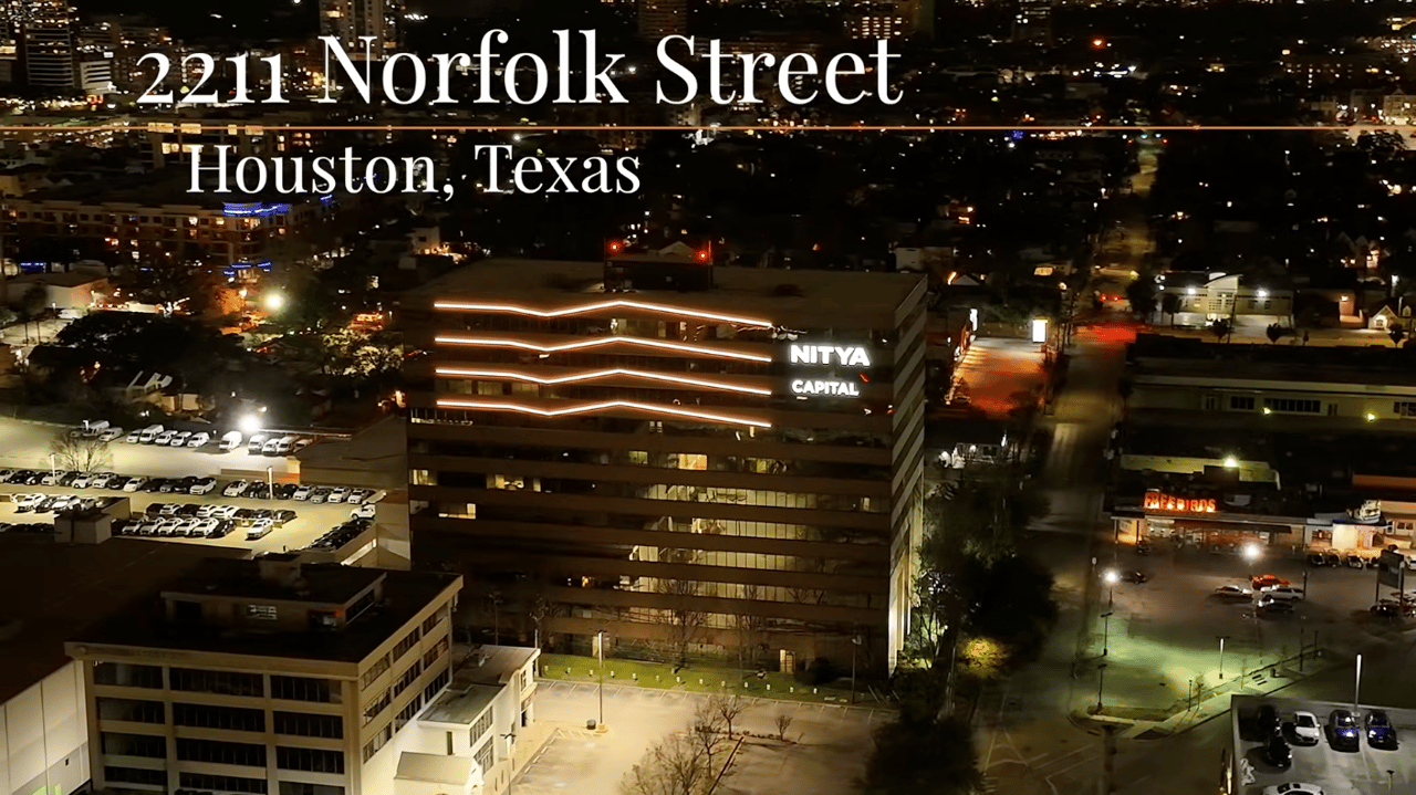 Aerial night view of 2211 Norfolk Street, a lit office building amid Houston parking lots.