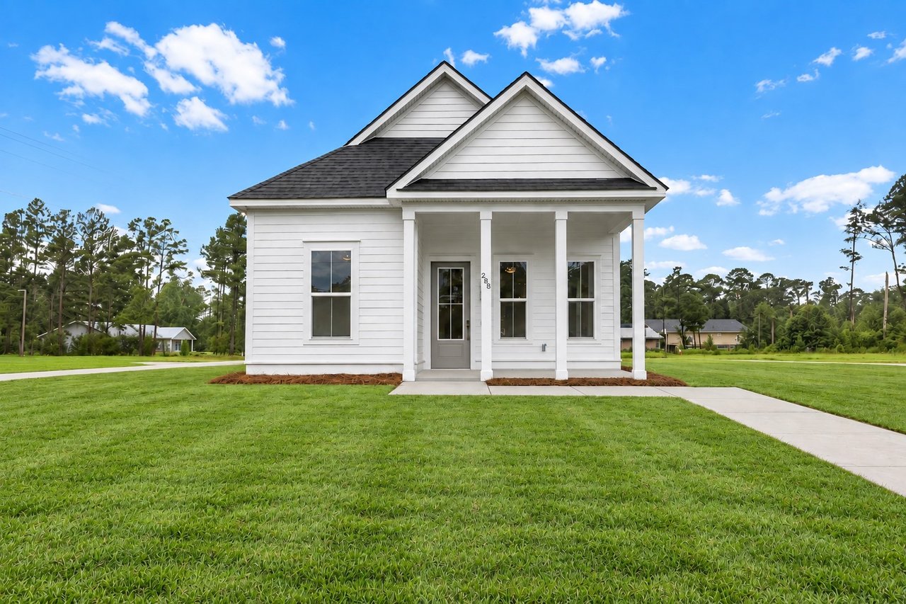 White home with a covered porch, steep gabled roof, and broad green lawn.