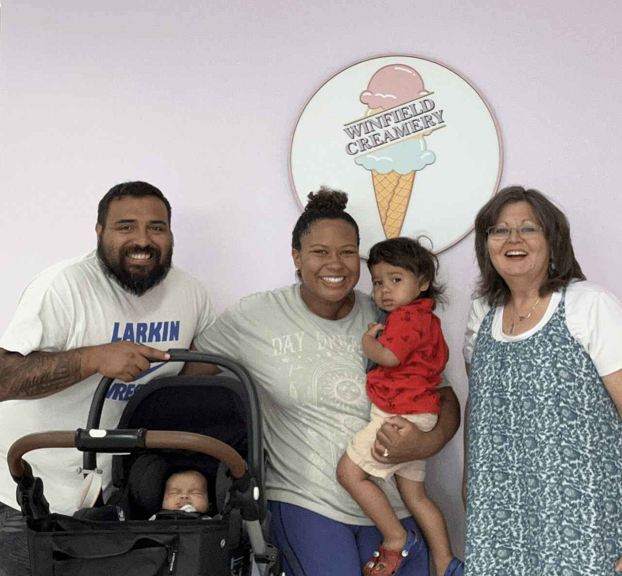 The smiling owners of Winfield Creamery pose with their toddler, baby, and blog author Faith Young under their logo.