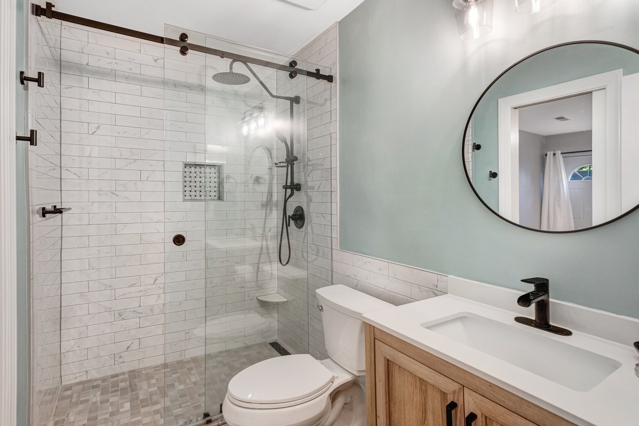 Bathroom with a glass-enclosed marble-look shower, white toilet, and wood vanity.