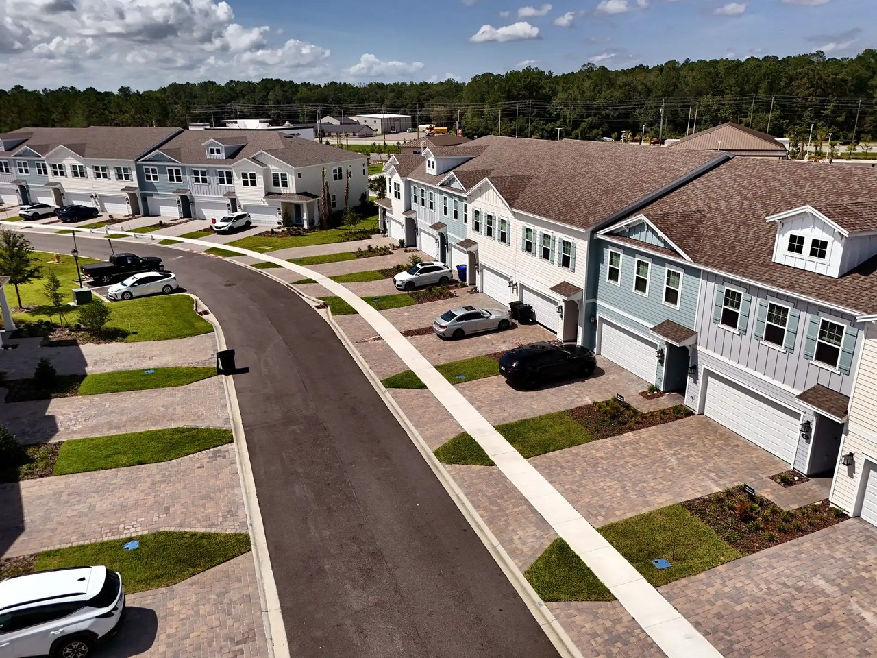 Aerial view of attached townhomes along a curved street, with garages, driveways, and landscaped lawns.