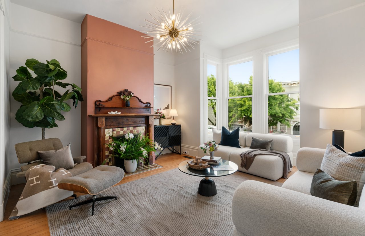 Living room with a vintage tiled fireplace, terracotta accent wall, white sofas, and tall windows.