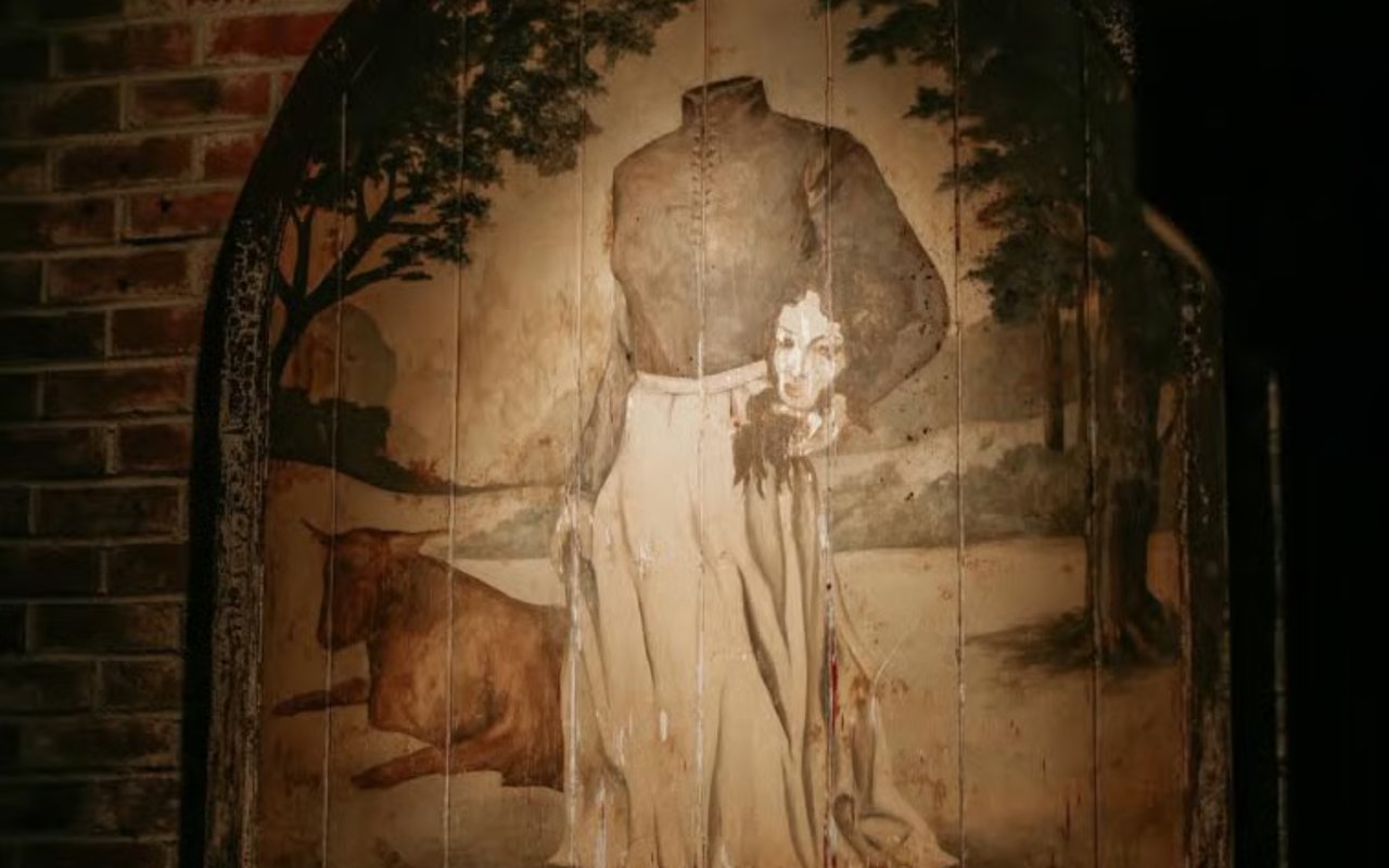 A weathered mural on a wooden arch, showing a headless figure holding a severed head, creates a dark mood.