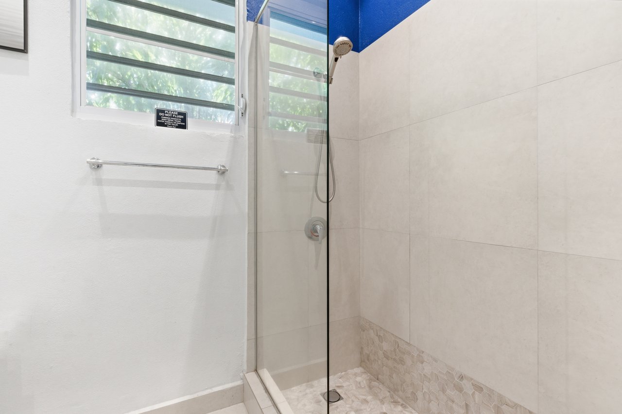 Bathroom shower with glass enclosure, pale tile, pebble floor, and a louvered window.