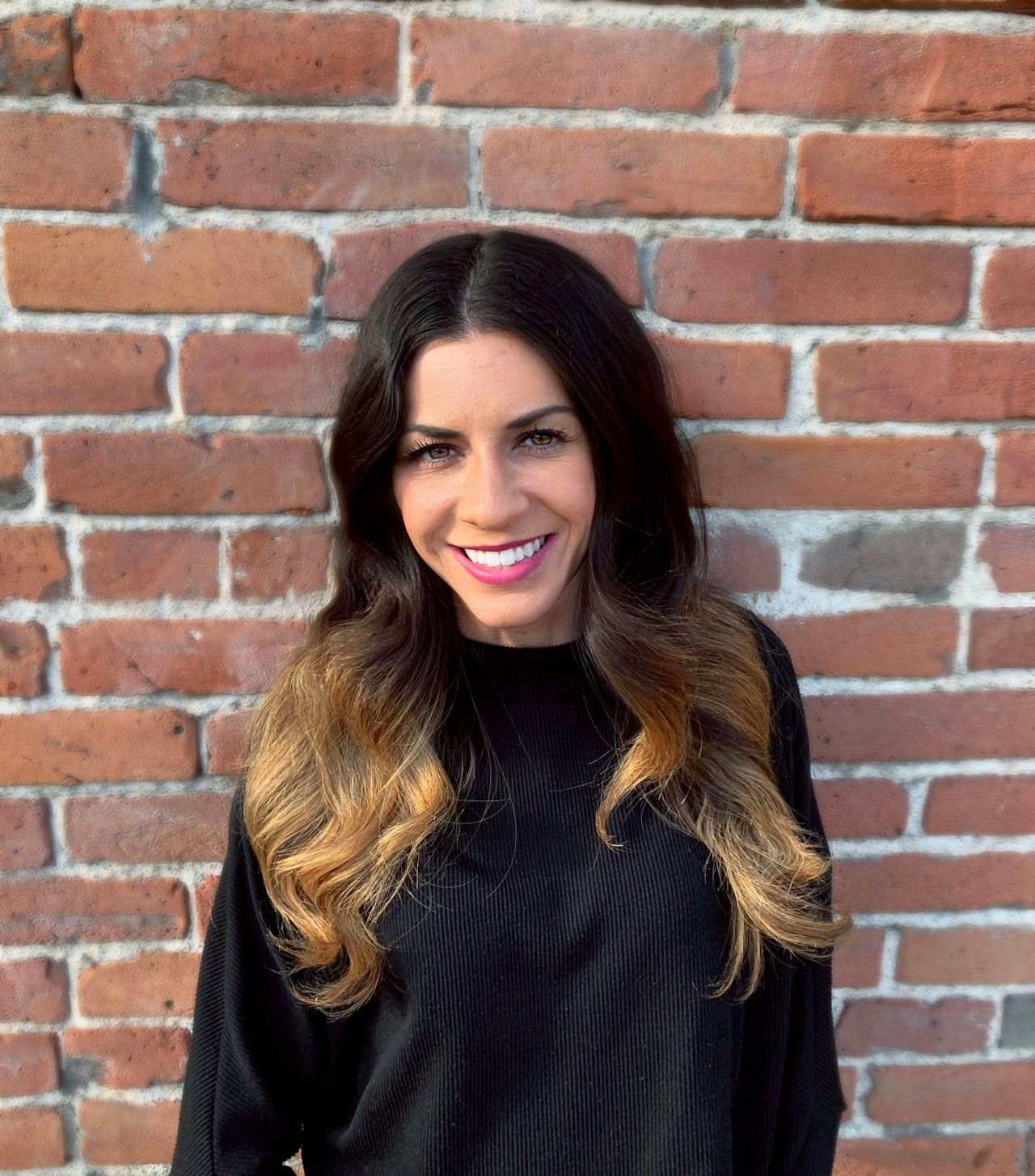 Lindsay Parente smiling in a black sweater in front of a brick wall.