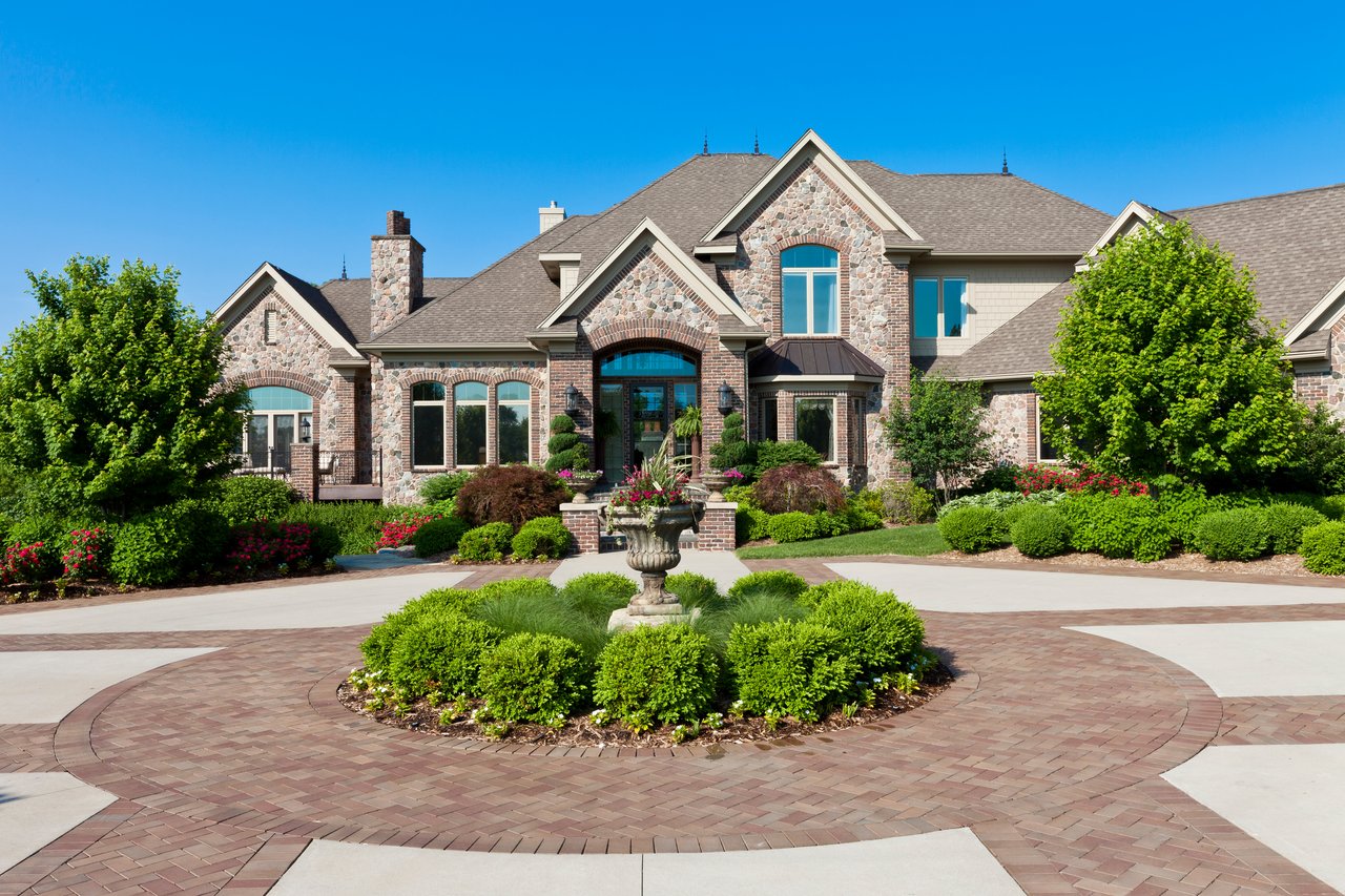 Large stone-and-brick house with a circular paved driveway and landscaped front garden.