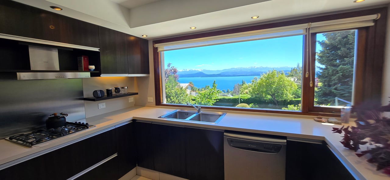 Modern kitchen with a wide window overlooking a lake and distant mountains.