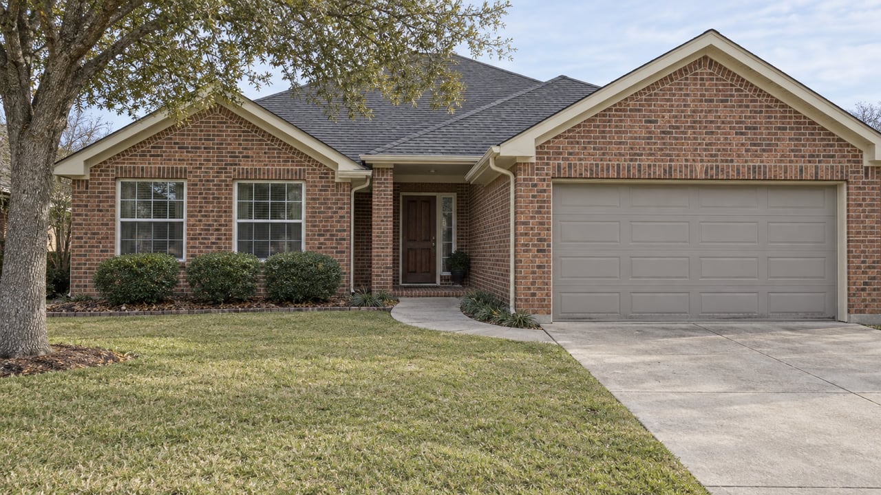 Single-story red-brick home with gabled roof, recessed entry, broad front lawn and a mature live oak in soft winter daylight.