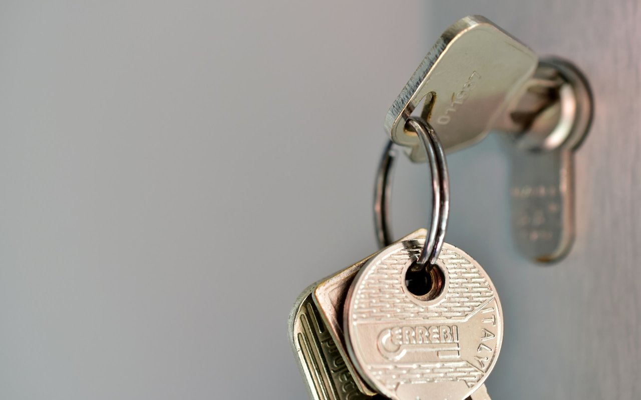 Metal keys on a ring, with a round brass key hanging from a key inserted into a lock.