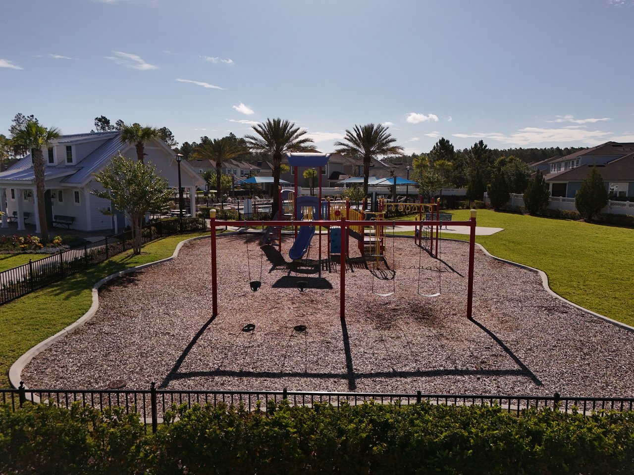 Community playground with swings and slides, surrounded by homes and palm trees.