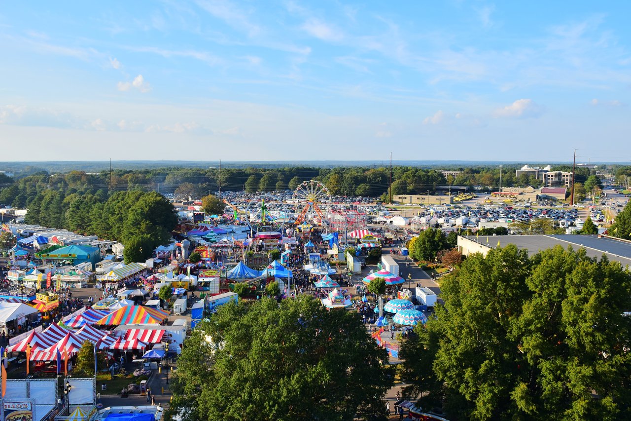 Aerial view of a crowded outdoor fair with colorful tents and a Ferris wheel.