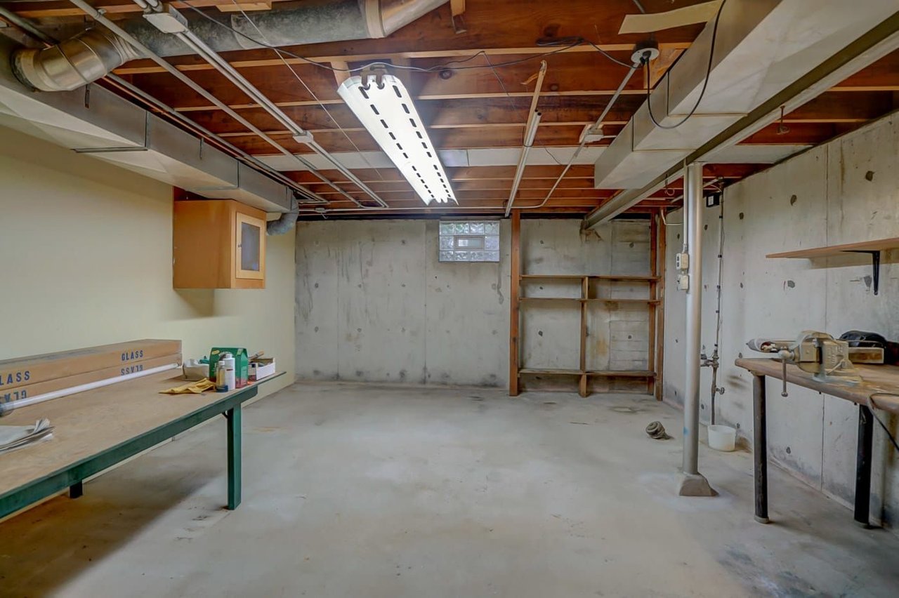 Basement workshop with exposed joists, concrete walls, shelving, and workbenches.