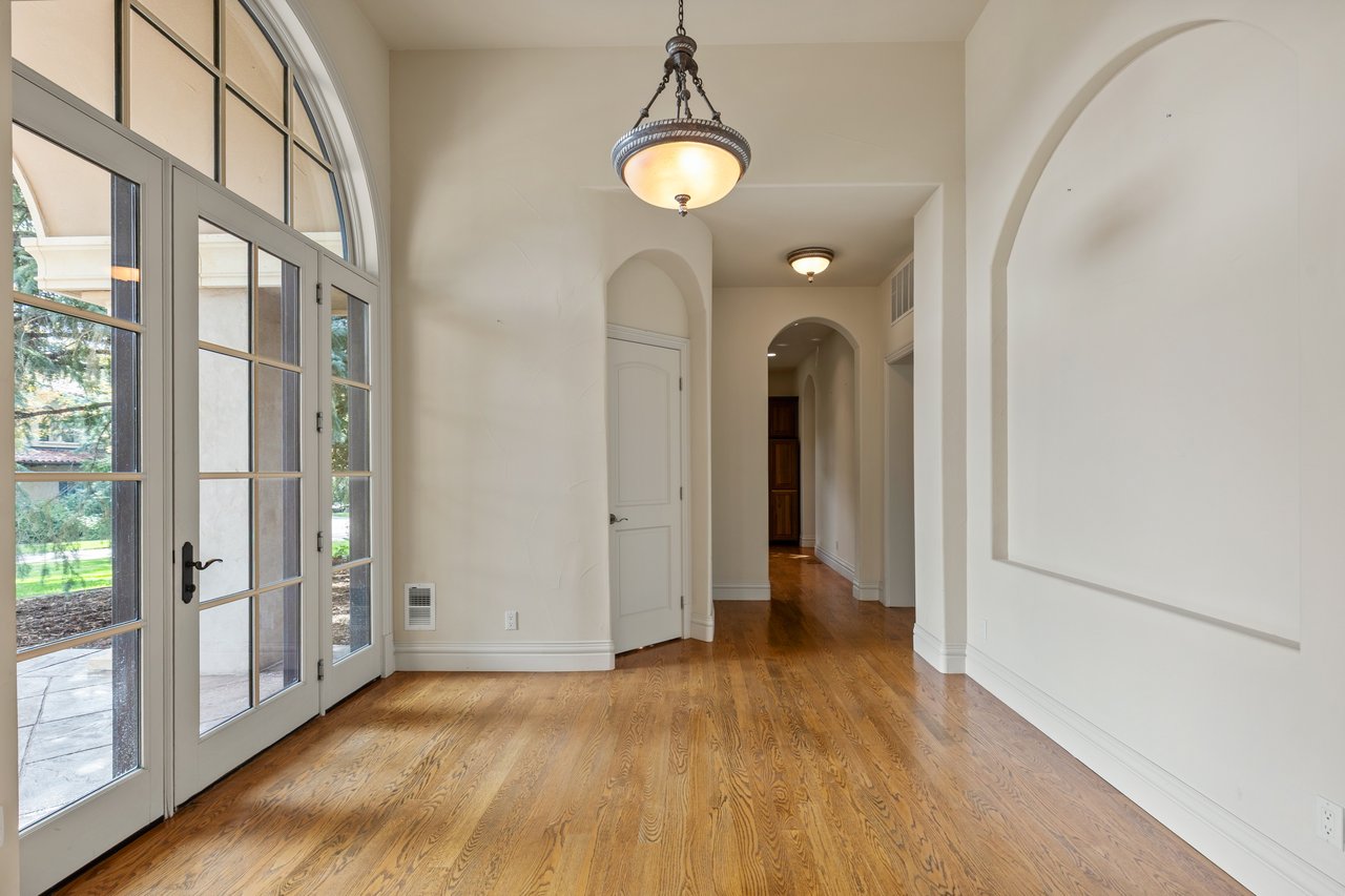 Empty entry hall with arched doorways, hardwood floors, and tall glass-paneled French doors.