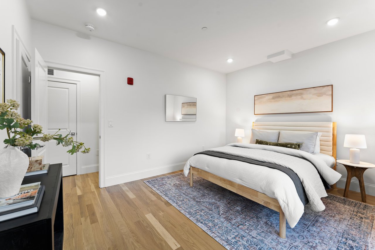 Bedroom with a white bed, abstract artwork, wood floors, and a patterned rug.