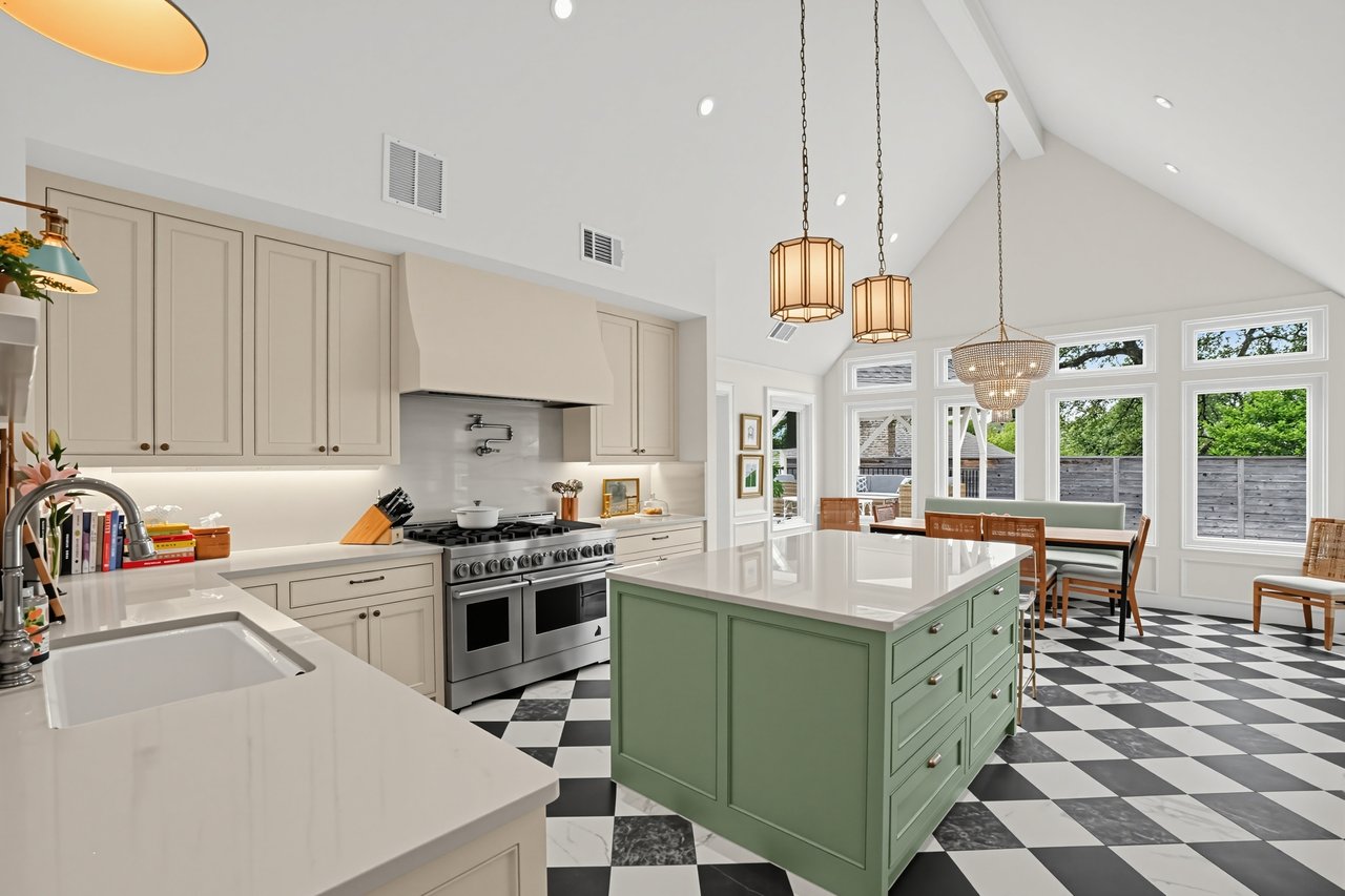 Open kitchen with a green island, checkerboard floor, and tall windows overlooking a fenced yard.