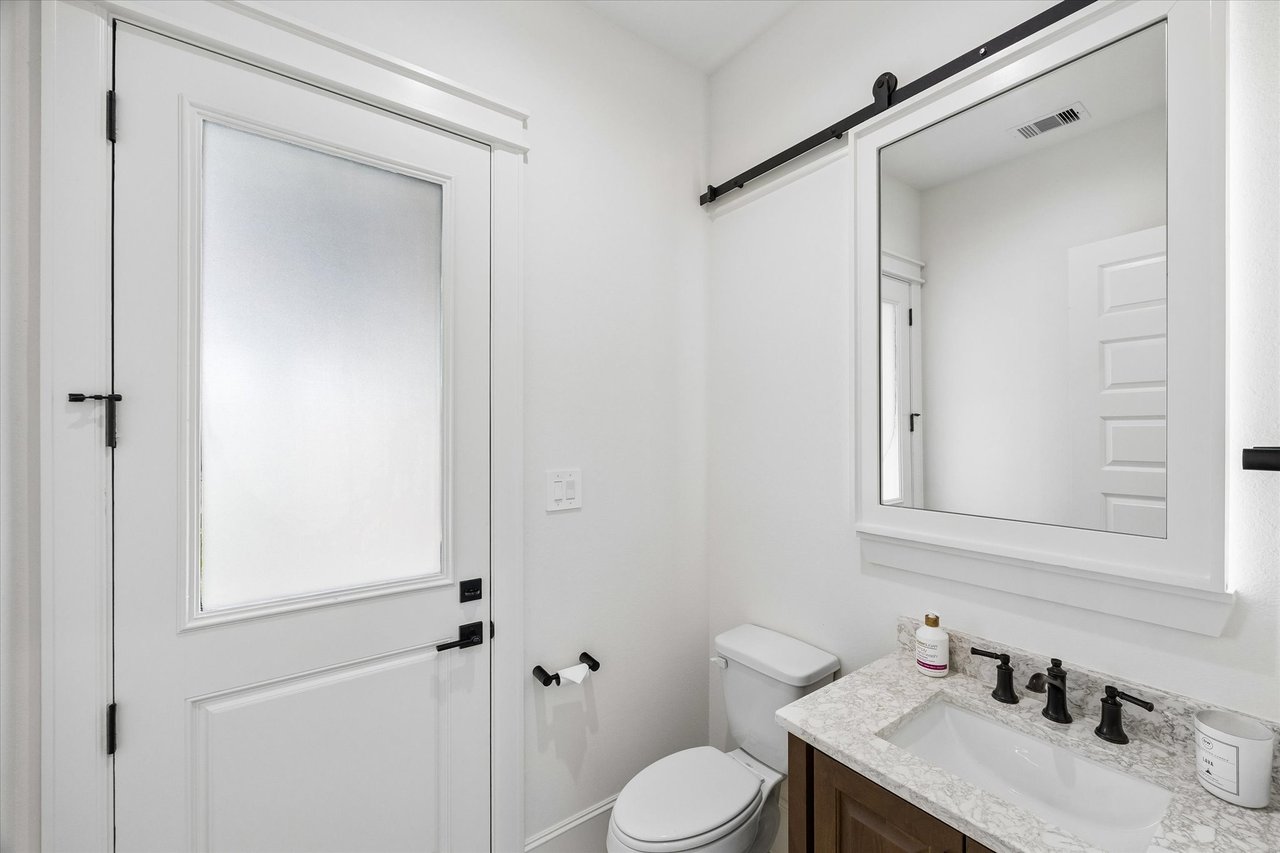 Bathroom with a wood vanity, marble-pattern countertop, black fixtures, and a frosted-glass door.