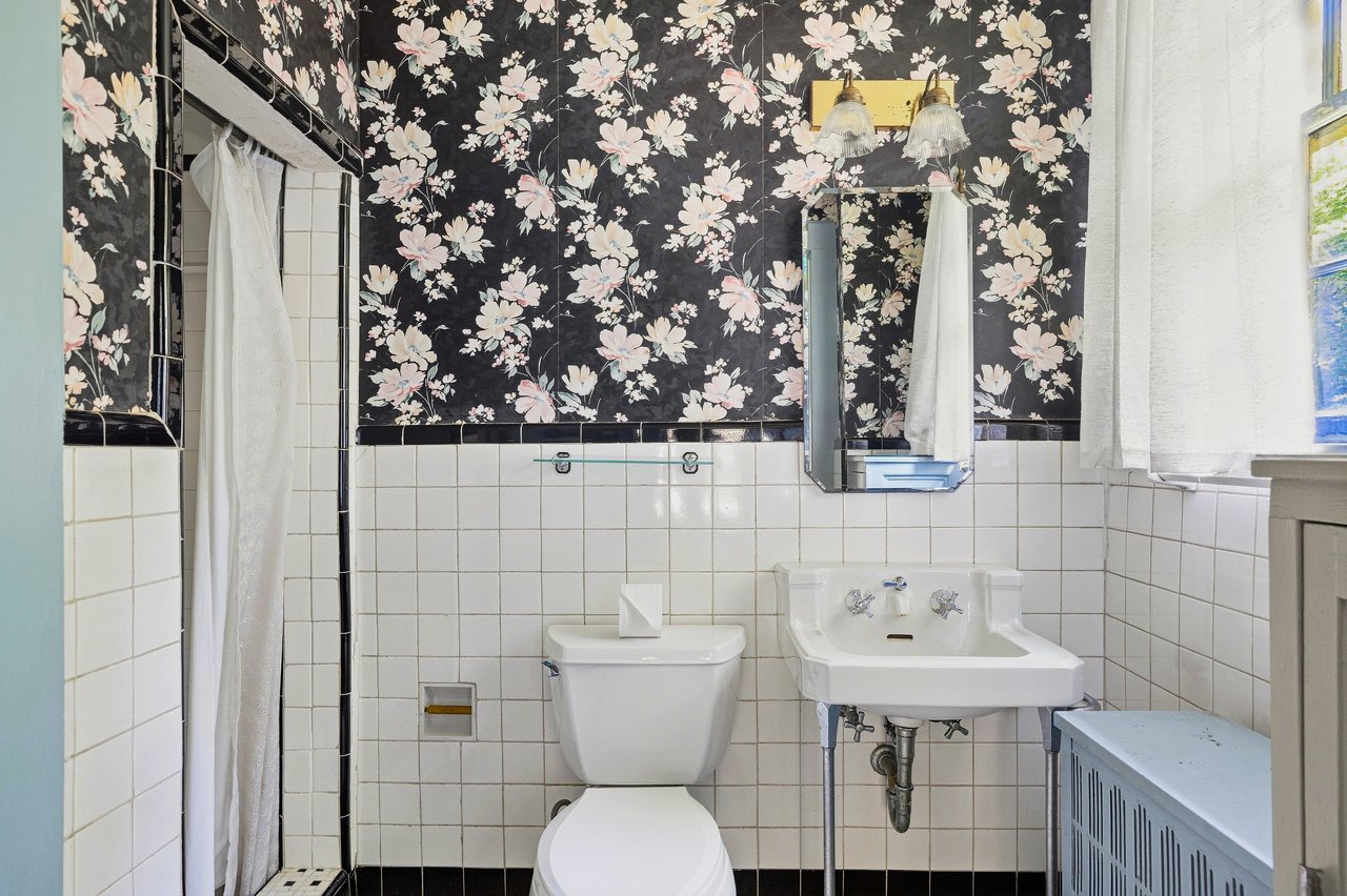 Bathroom with floral wallpaper, white tile, a toilet, pedestal sink, and curtained shower.