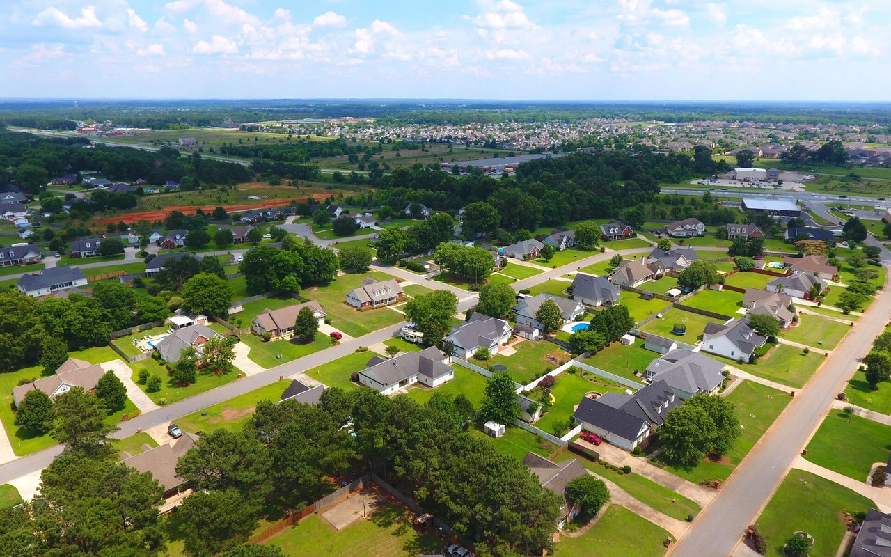 Aerial view of a suburban neighborhood with detached homes, tree-lined streets, and green lawns.