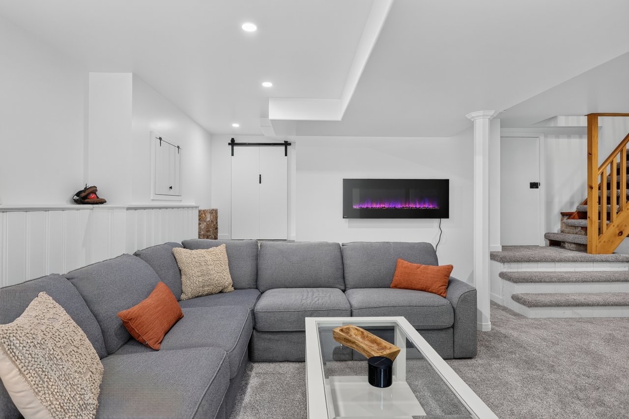 Living area with a gray sectional, purple-lit electric fireplace, and carpeted stairs.