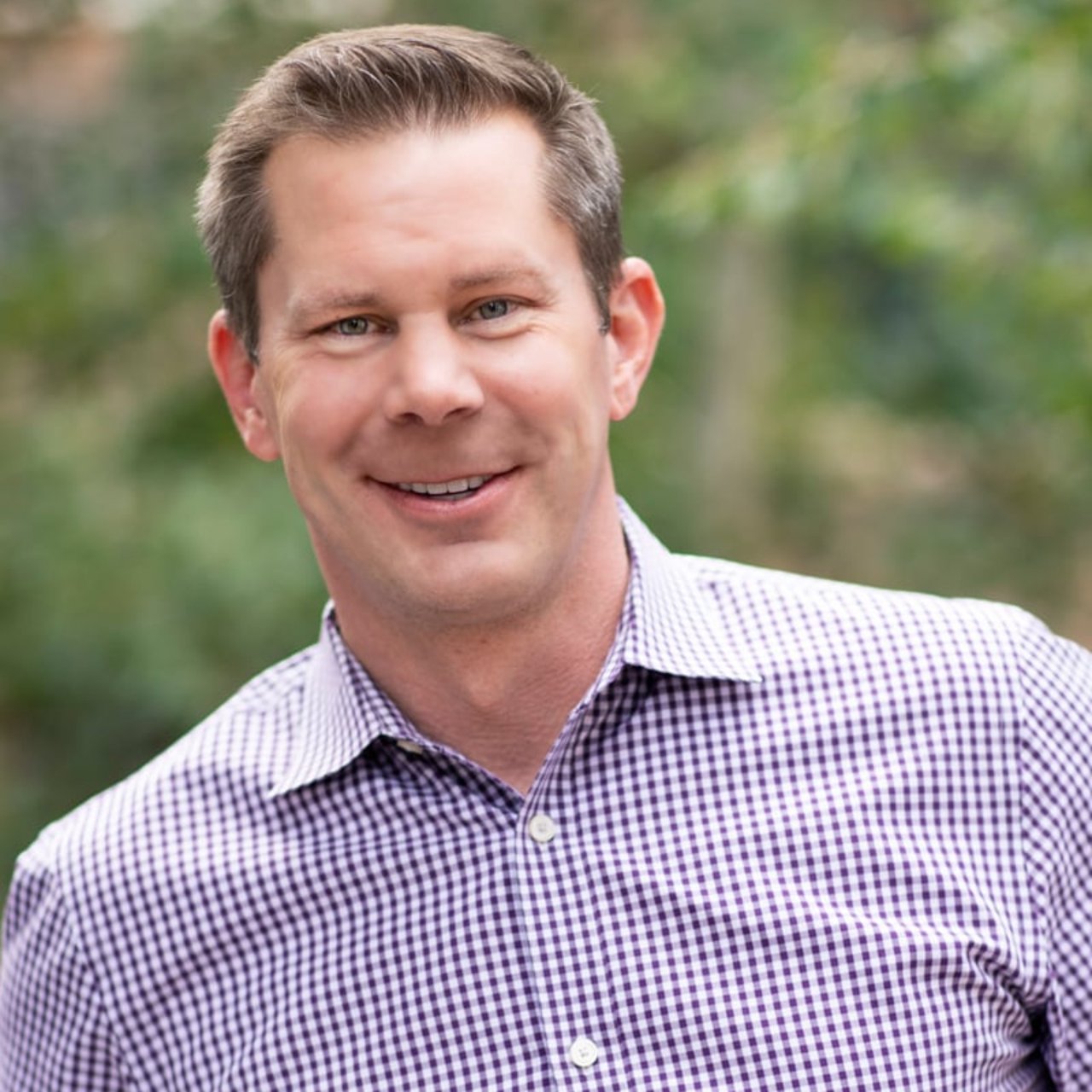 Ford Fuller in a purple-and-white checkered shirt against a blurred green background.