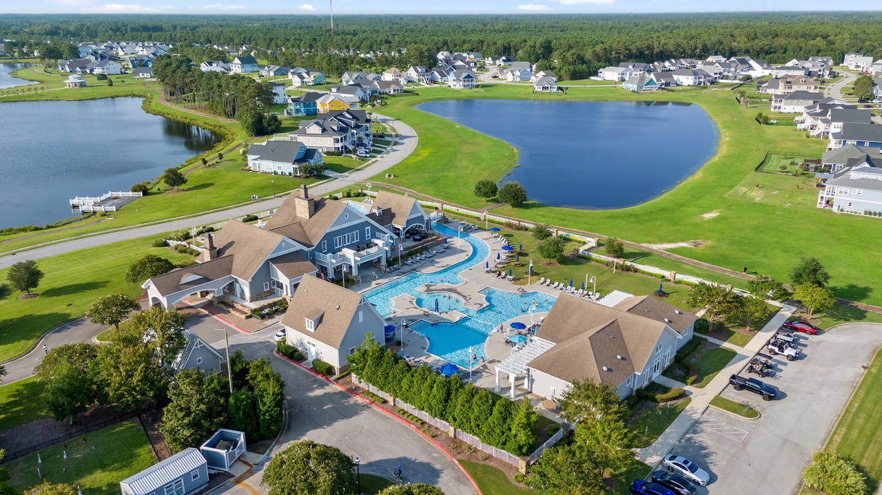 Aerial view of a residential community with a clubhouse, swimming pools, lakes, and surrounding homes.