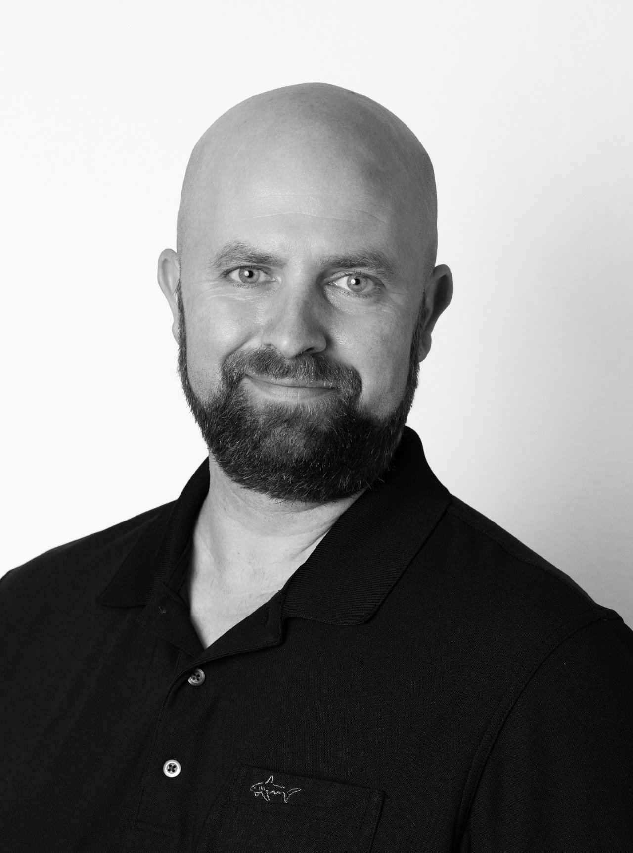 DJ Braden, a bald real estate agent with a full beard, wearing a dark collared shirt.