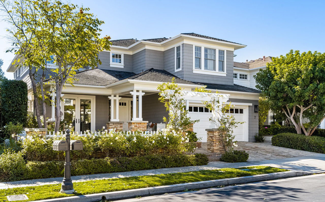 Two-story gray-shingled home with white trim, a covered entry, attached garage, and landscaped front garden.