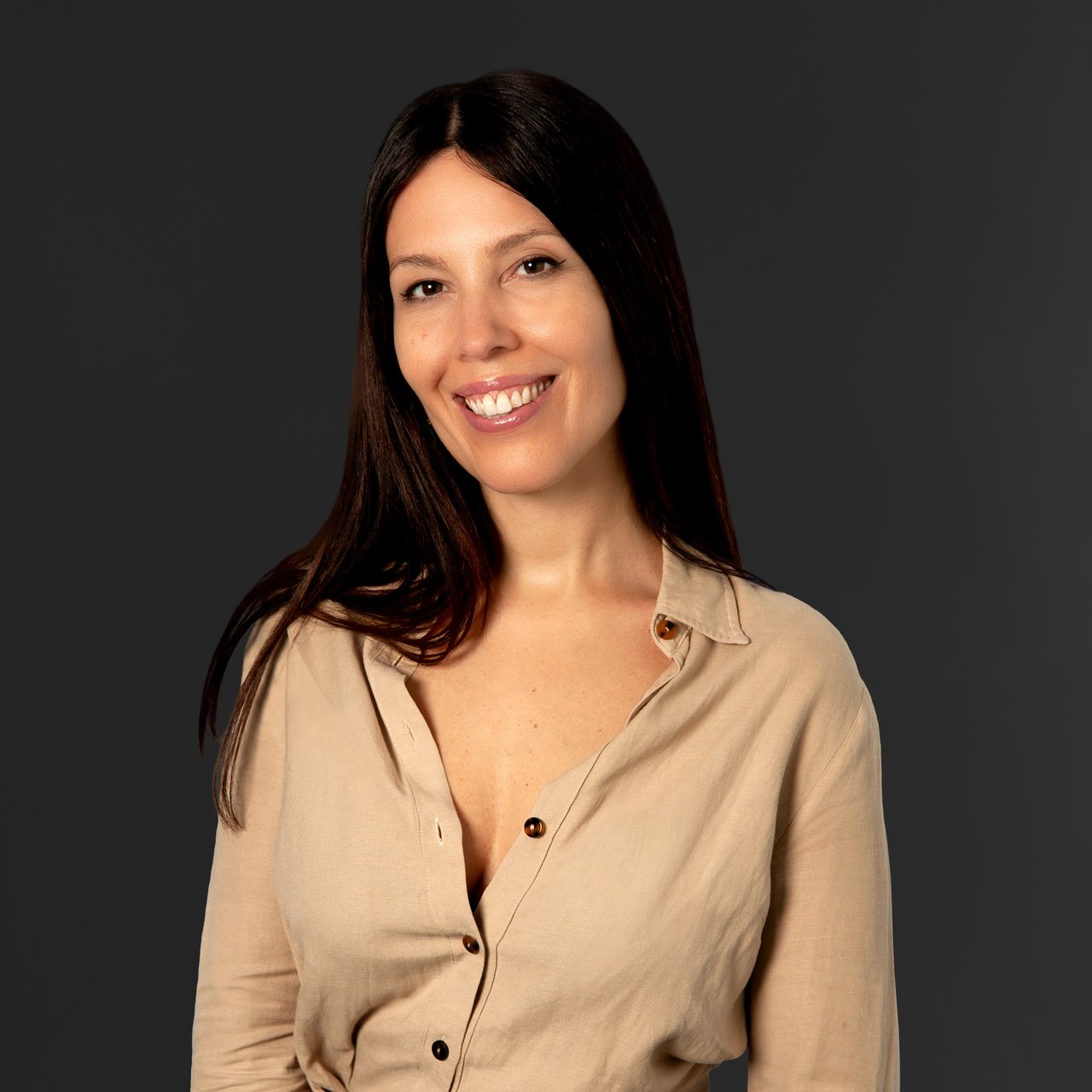 Ava McLeod smiling in a beige blouse against a dark background.
