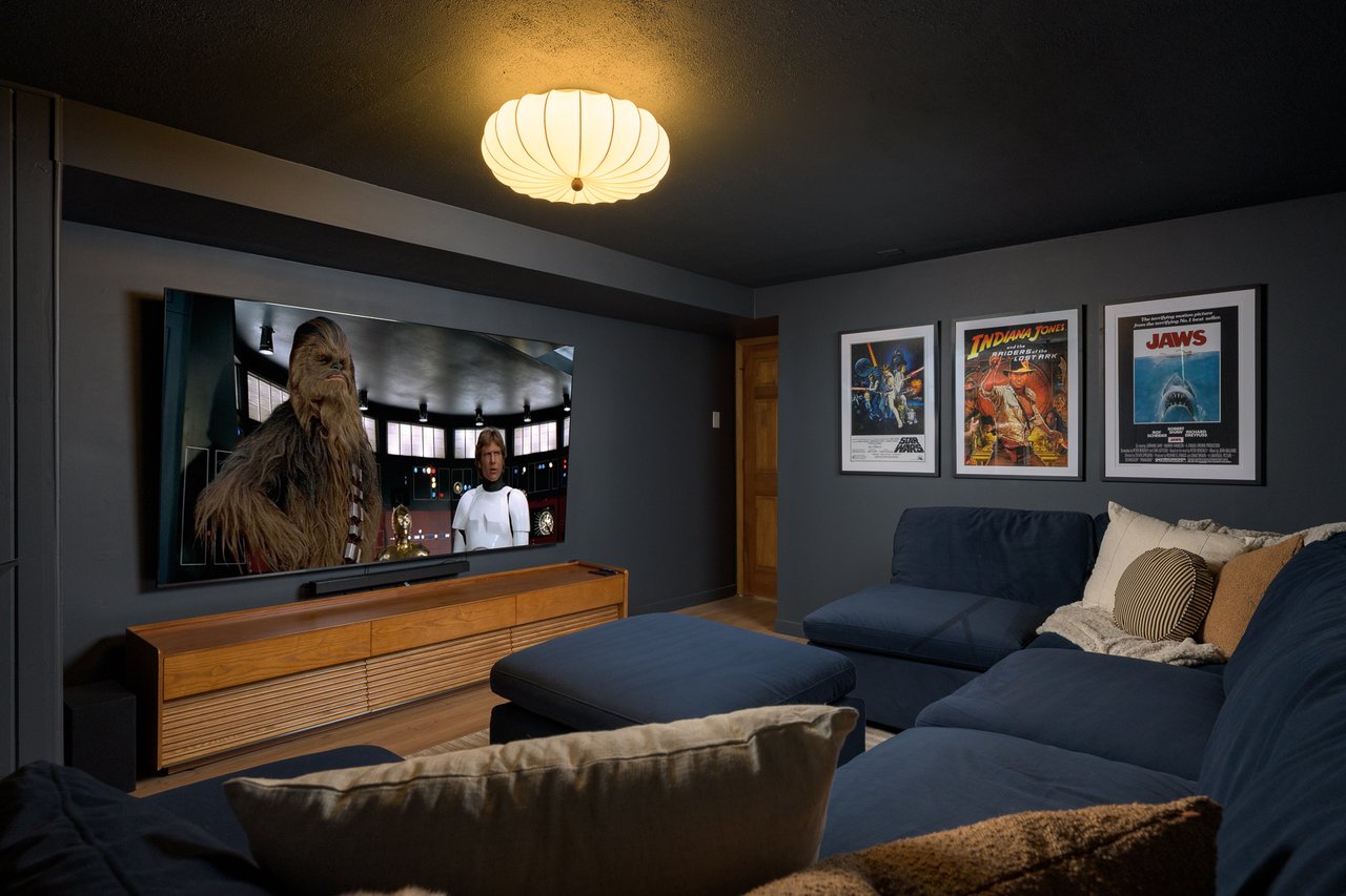 Home theater with a large television, blue sectional sofa, wooden media console, and framed movie posters.