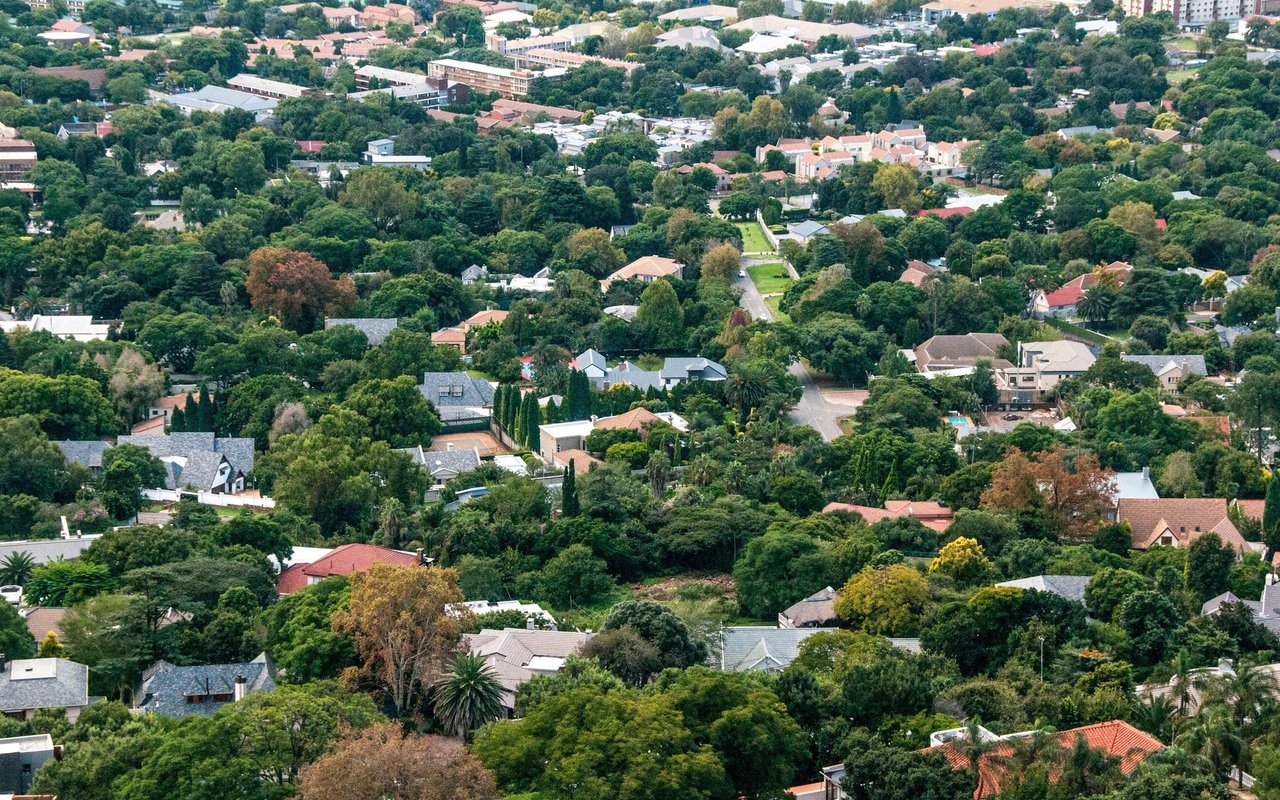 Aerial view of a leafy residential neighborhood with varied homes and apartment buildings in the distance.