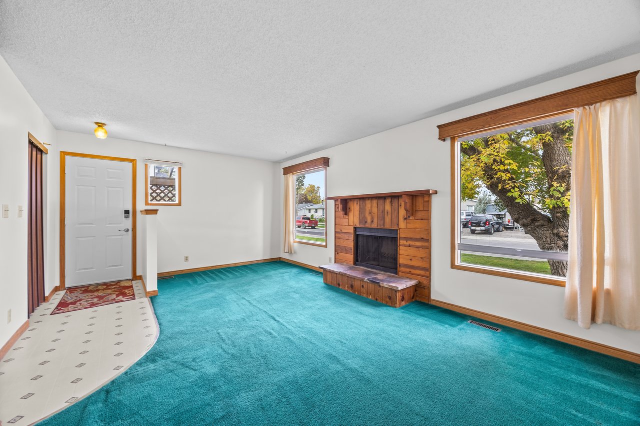 Living room with turquoise carpet, a built-in wooden fireplace, and large windows.