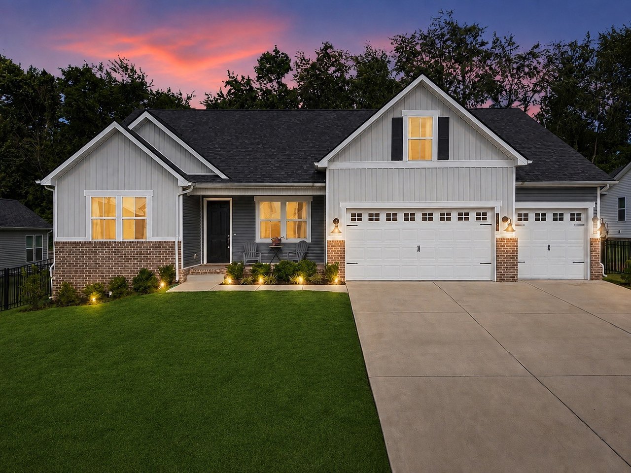 Gray two-story home with brick accents, double garage, broad driveway, and lawn at dusk.