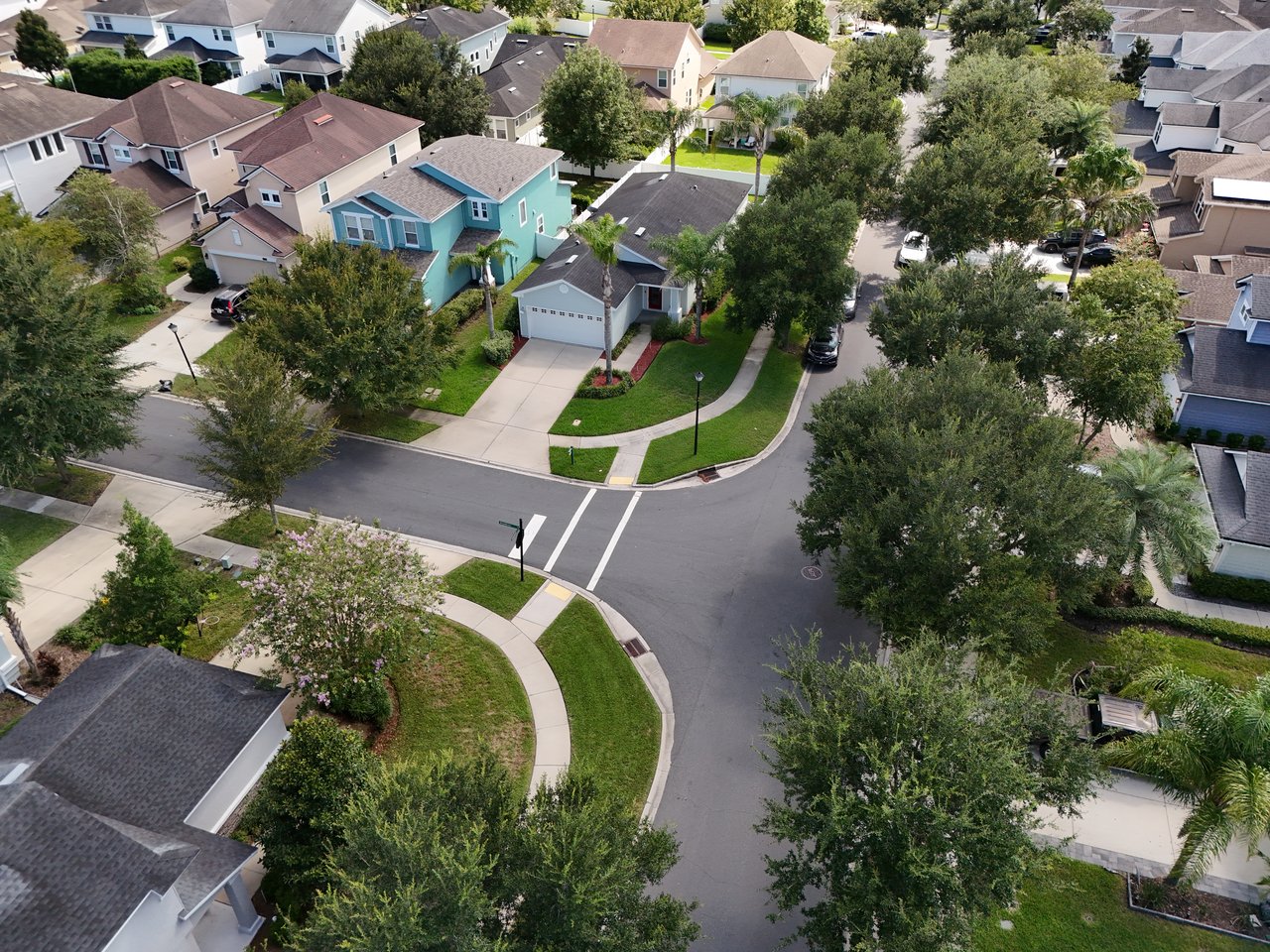 Aerial view of a leafy neighborhood with detached homes and a residential street intersection.