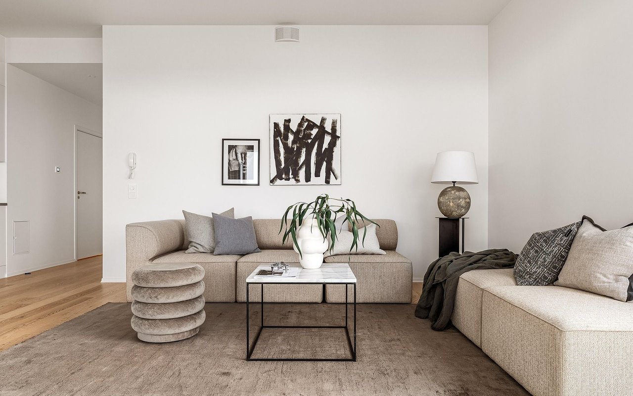 Furnished living room with beige sofas, abstract art, and a marble-topped coffee table.