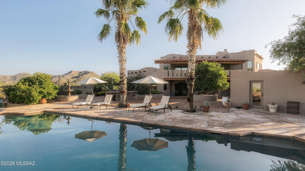 Southwestern-style home beside a swimming pool, with palm trees and mountains in the background.
