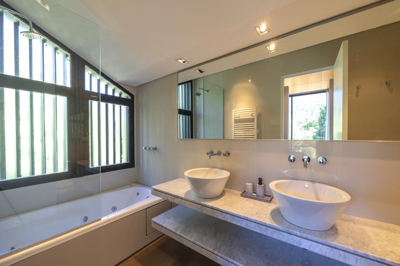 Modern bathroom with a built-in tub, two vessel sinks, and tall black-framed windows.