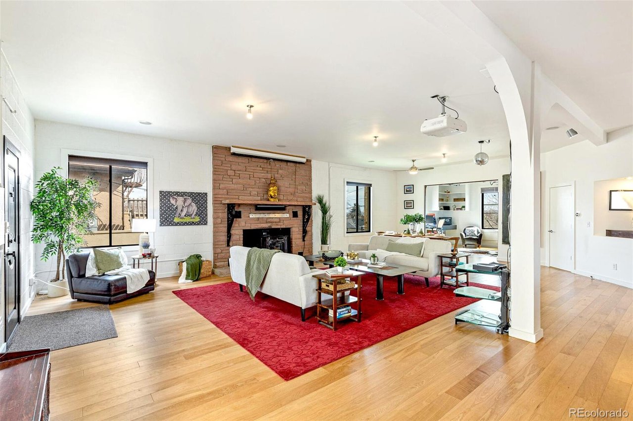 Open-plan living room with a brick fireplace, white sofas, red rug, and hardwood floors.