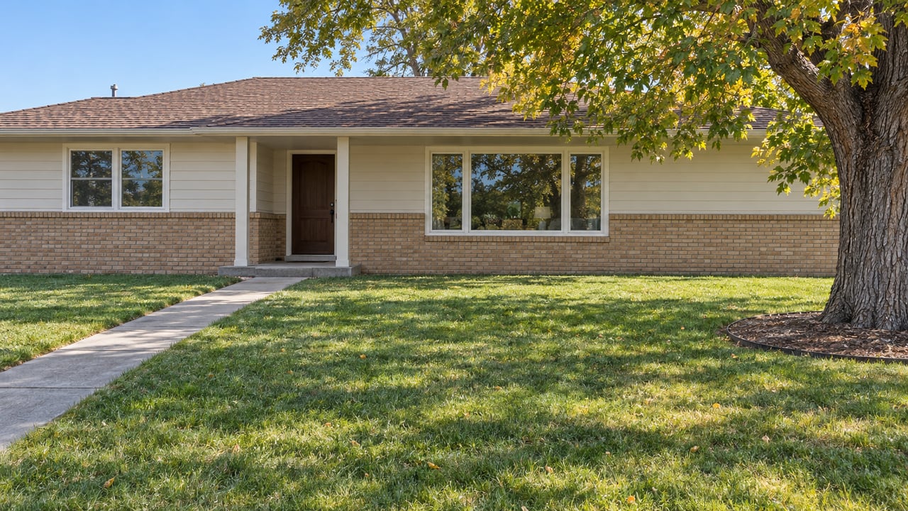 Single-story brick-and-siding ranch behind a broad autumn lawn, with a concrete entry walk and mature cottonwood.