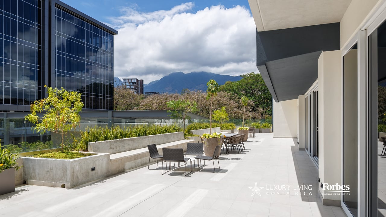 Penthouse terrace with outdoor seating, raised planters, modern buildings, and mountain views.